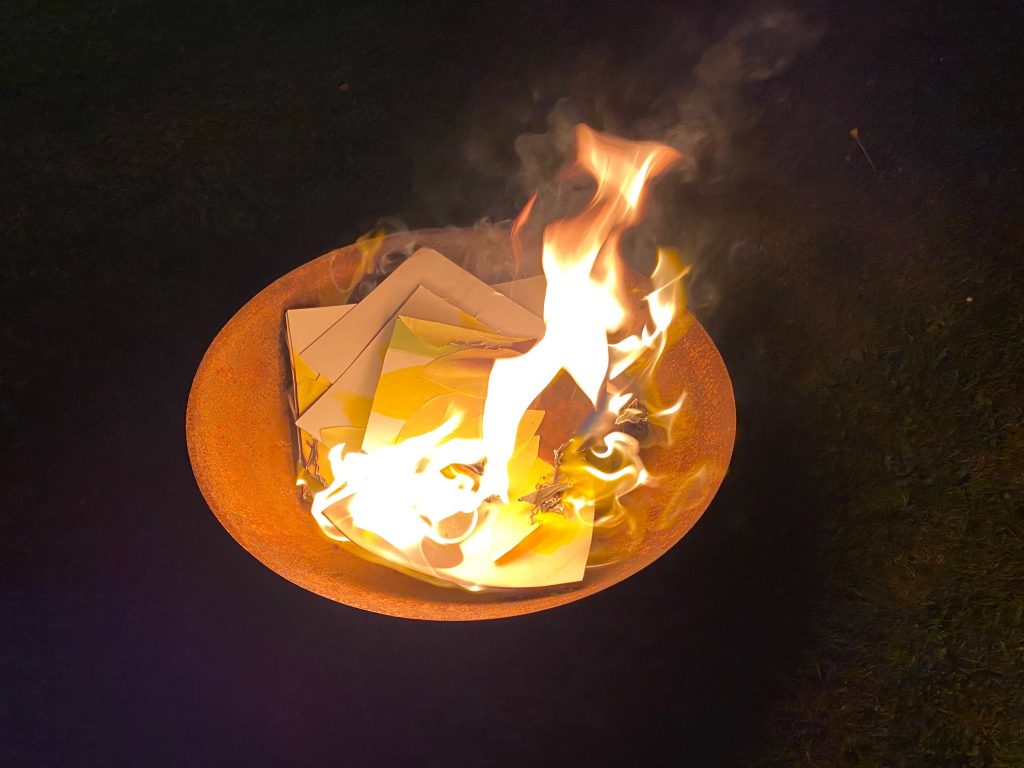 a round firepit bowl, with paper in it. The paper is on fire, with smoke swirling above the fire.