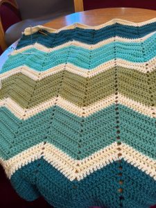 a large amount of crochet (it's the start of a blanket), zig zag stripes in various shades of green with thinner white zig zags in between each shade of green.